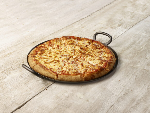 Cheese pizza in a black pan with handles on each side on a whitewashed wood background