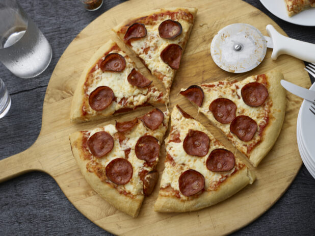 Sliced pepperoni pizza, one slice removed, on a wood pizza peel, black background, overhead view