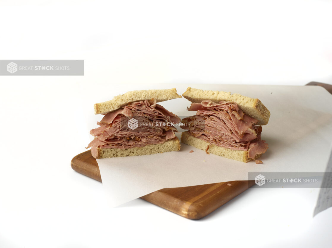 Corned beef sandwich on light rye, cut in two on white parchment on a wood cutting board