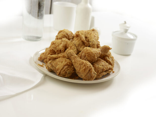 Deep fried chicken pieces piles on a round white plate, white table setting, white background