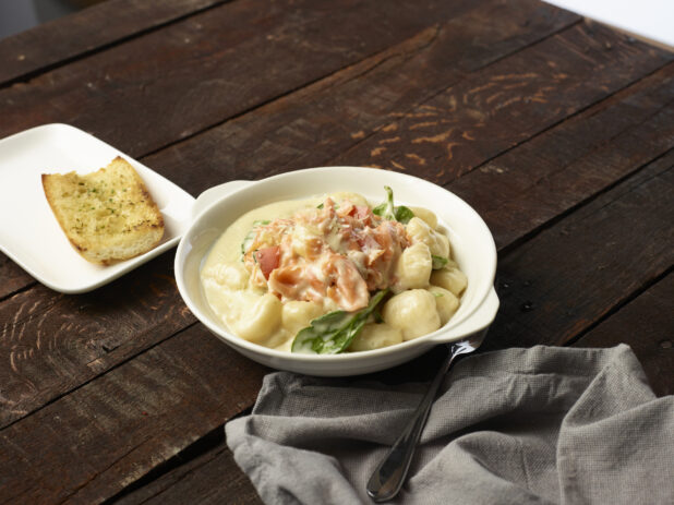Baking dish of creamy salmon gnocchi with a side of garlic bread and cloth napkin on a dark wooden background83392