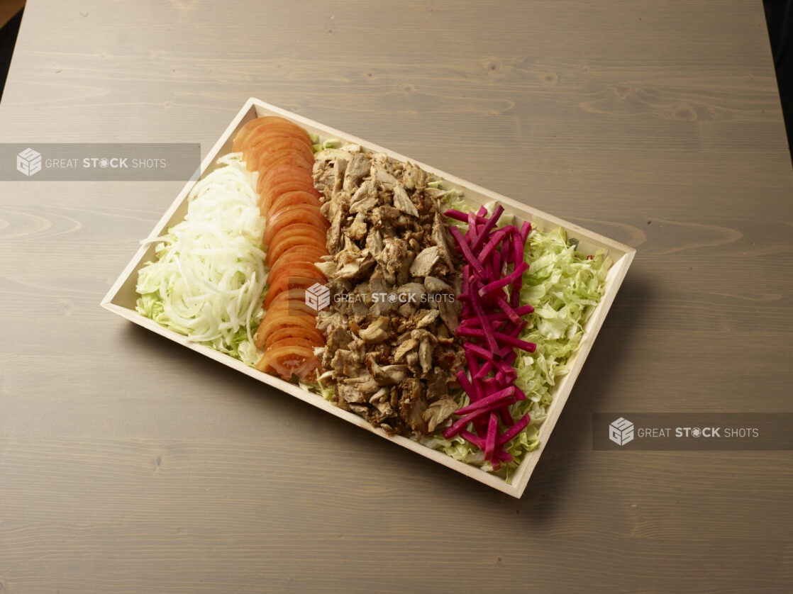 Overhead view of a wooden platter with sliced, onion, tomatoes, turnip and chicken shawarma meat on a wooden background