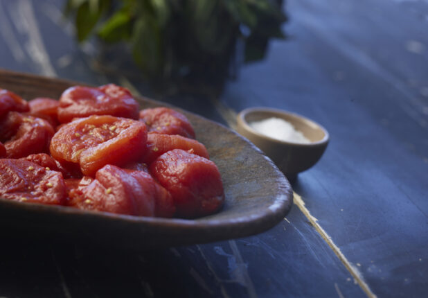 Drained San Marzano tomatoes on a rustic dark pottery plate, bowl of salt and basil in background, close-up