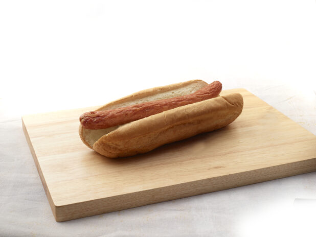 Plain hotdog on a bun on a wooden cutting board, white background, close-up