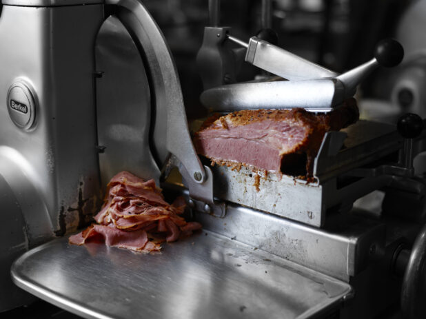 Corned beef being sliced in a commercial meat slicer, close-up