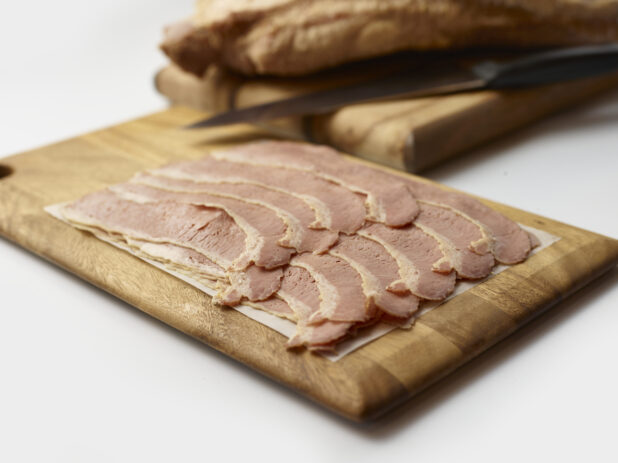 Thin slices of corned beef arranged on a wood board, background objects, white background