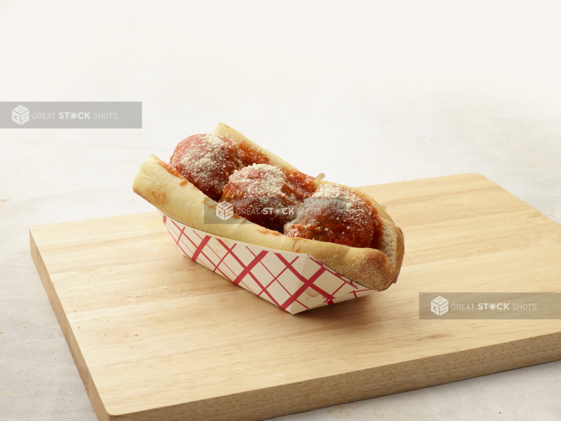 Three large meatballs with tomato sauce and a sprinkle of parmesan on a wood board, light background