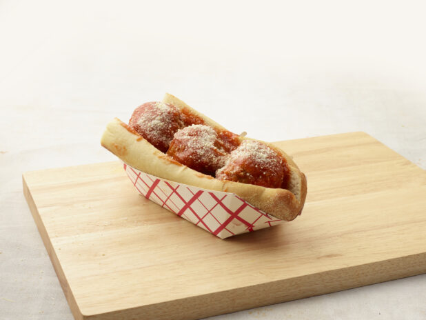 Three large meatballs with tomato sauce and a sprinkle of parmesan on a wood board, light background