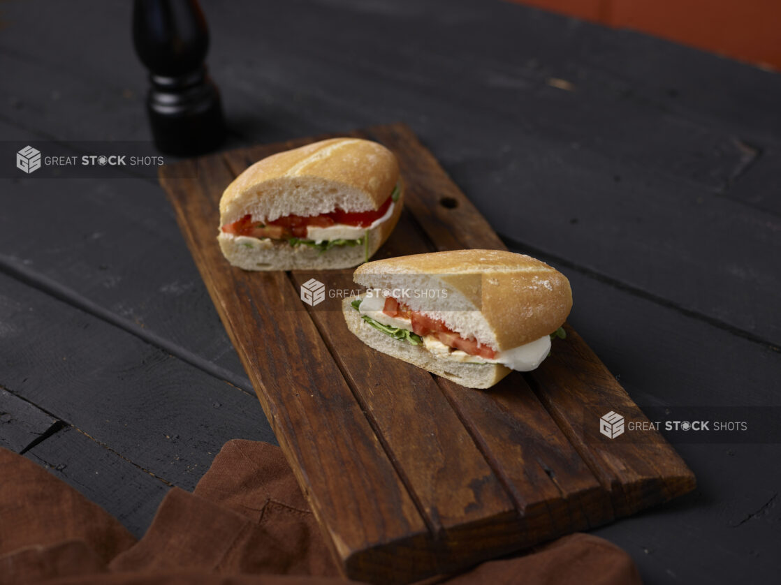 Caprese sandwich on a sliced white bun on dark wooden board, dark background