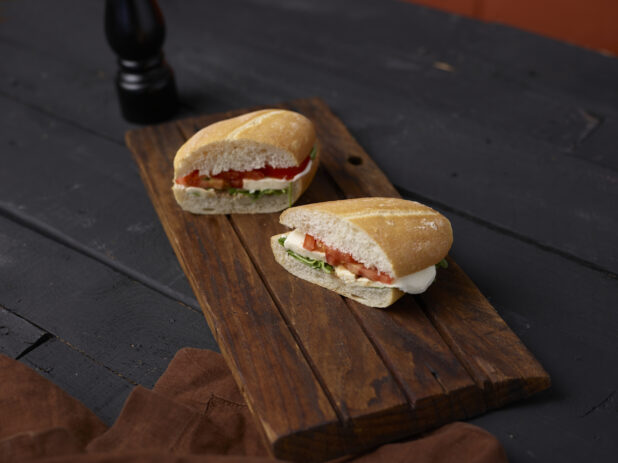 Caprese sandwich on a sliced white bun on dark wooden board, dark background