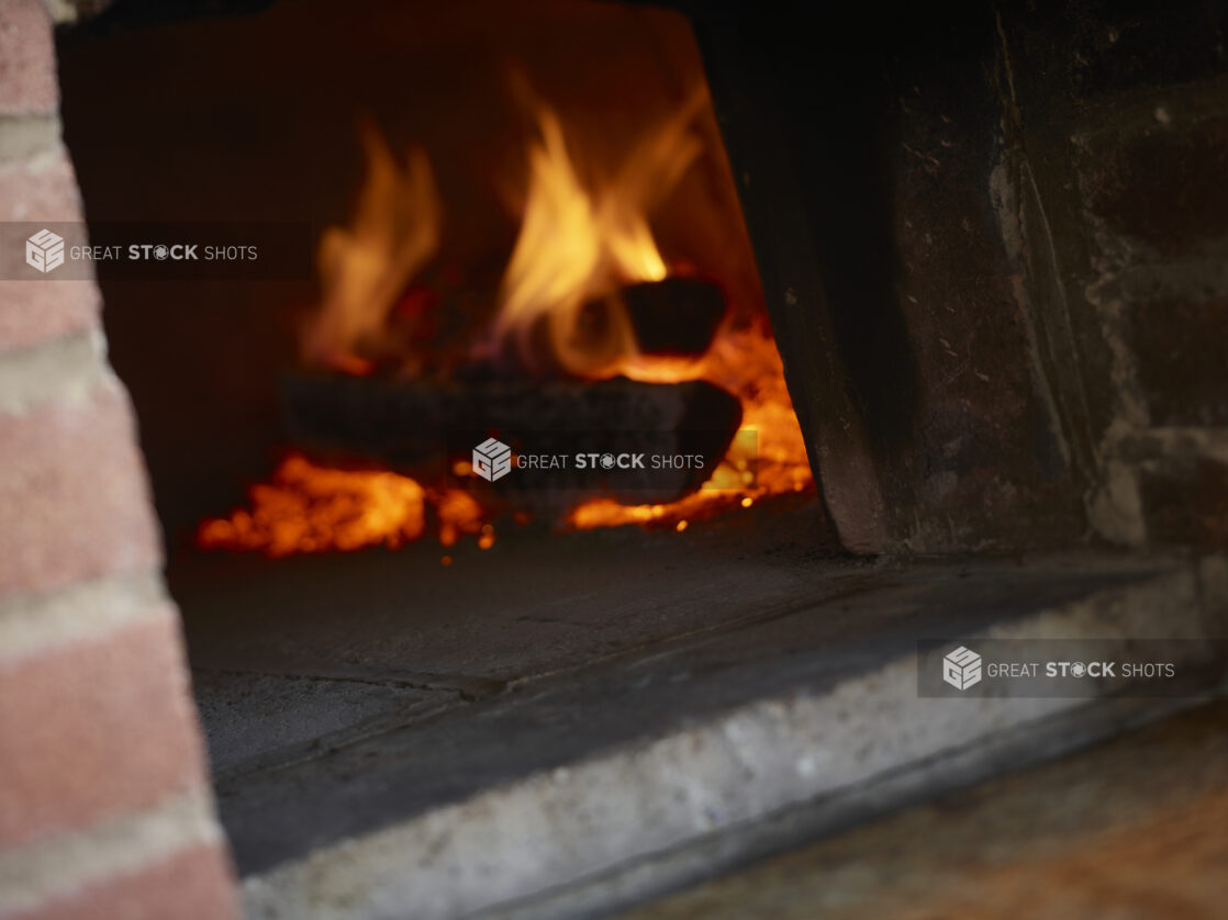 Logs on fire and embers inside a wood burning pizza oven