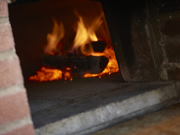 Logs on fire and embers inside a wood burning pizza oven