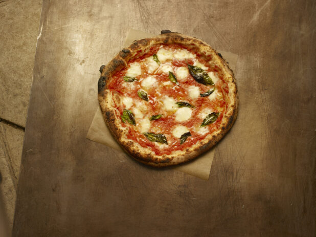 Whole Neapolitan-style Margherita pizza on parchment, wood background, overhead
