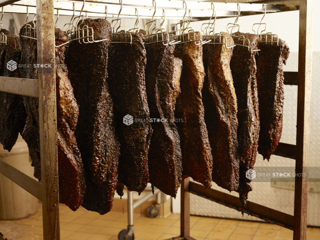 Smoked meat hanging from hooks on a wood frame in a commercial setting