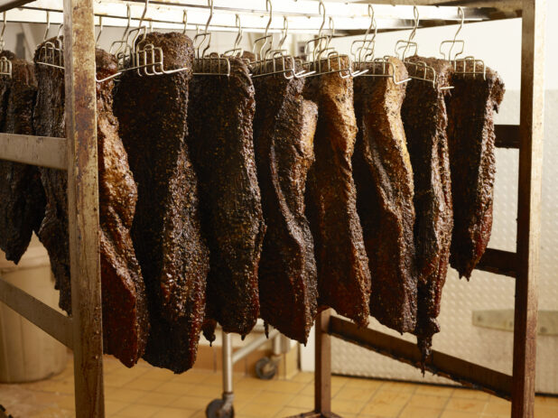Smoked meat hanging from hooks on a wood frame in a commercial setting