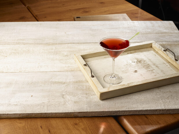 Red cocktail in a martini glass with a sugared rim and maraschino cherry garnish