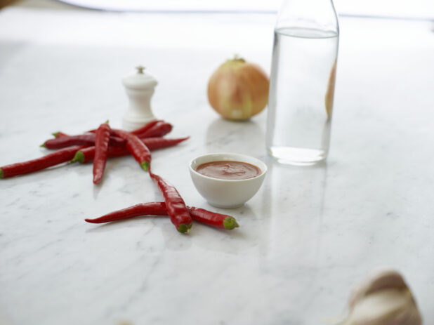 Long red chilis with a ramekin of red sauce, white marble background