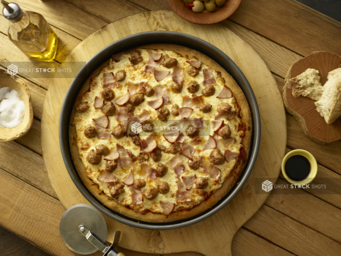 Whole deep dish meat pizza in a pan on a wooden background with ingredients