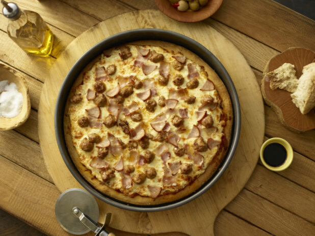 Whole deep dish meat pizza in a pan on a wooden background with ingredients