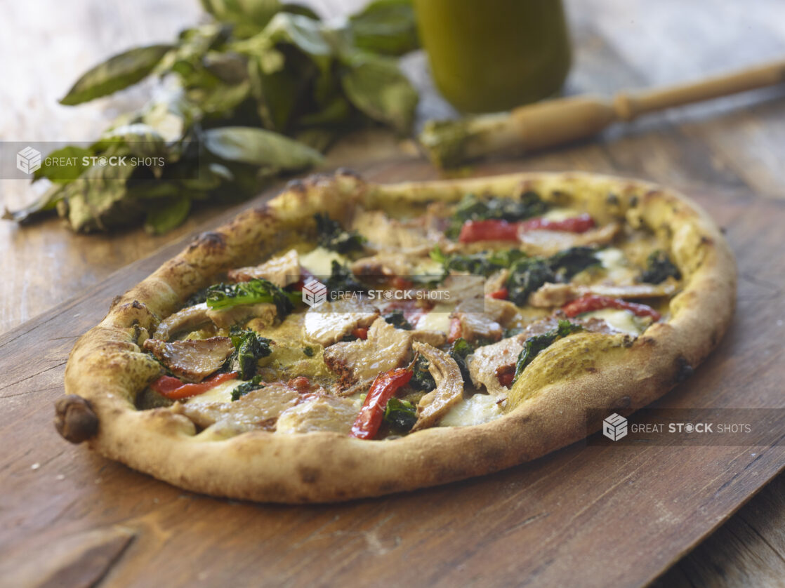 Whole pizza with pork, roasted red peppers, and kale on a wood board, close-up, low angle