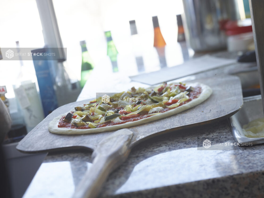 Unbaked pizza on a wood pizza peel on a marble work surface, low angle