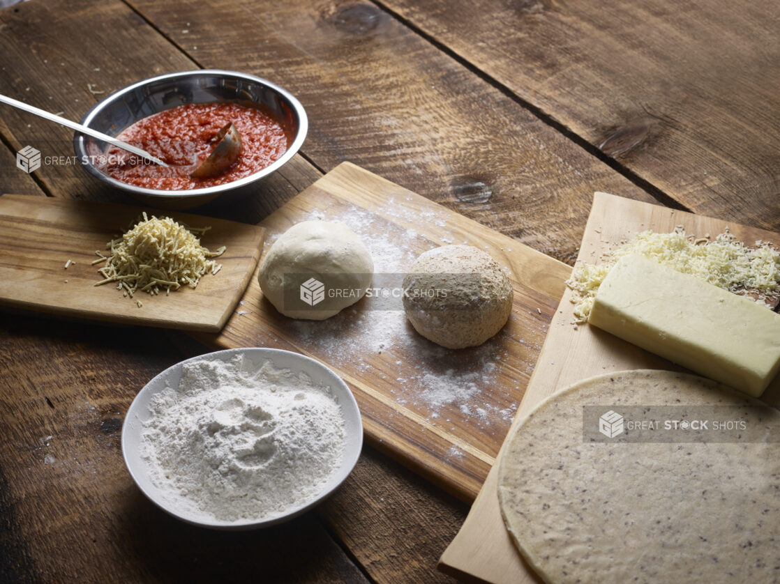 Dough balls and ingredients to make regular and gluten-free pizzas on wooden boards on a wooden background