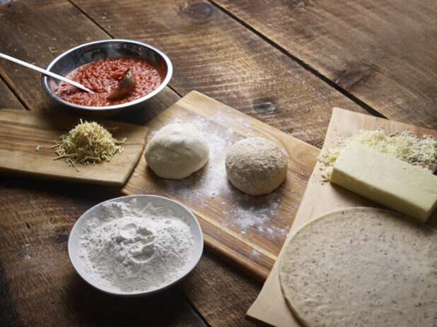 Dough balls and ingredients to make regular and gluten-free pizzas on wooden boards on a wooden background