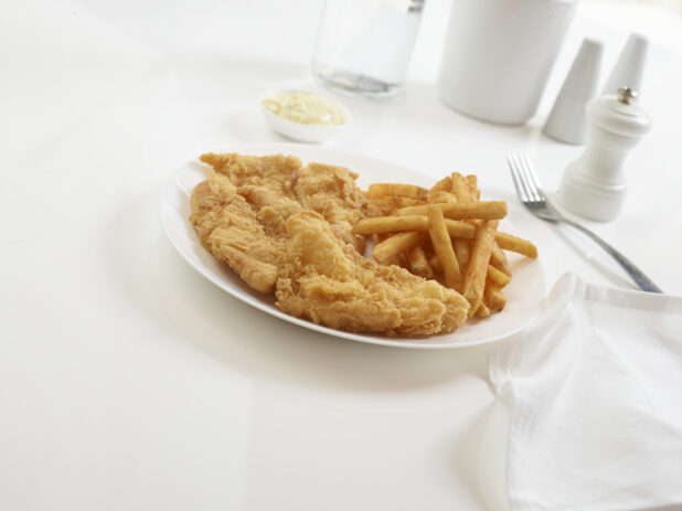 Plate of fish and chips with a side of tartar sauce on a white background