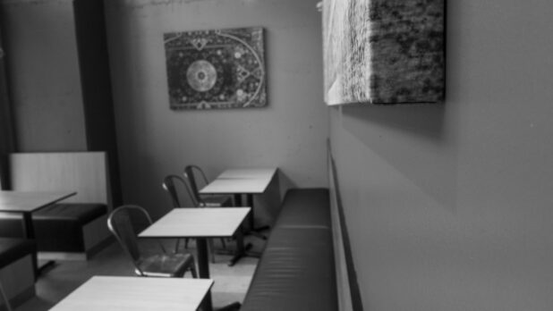 Black and white interior of an empty restaurant with seating and artwork on the wall