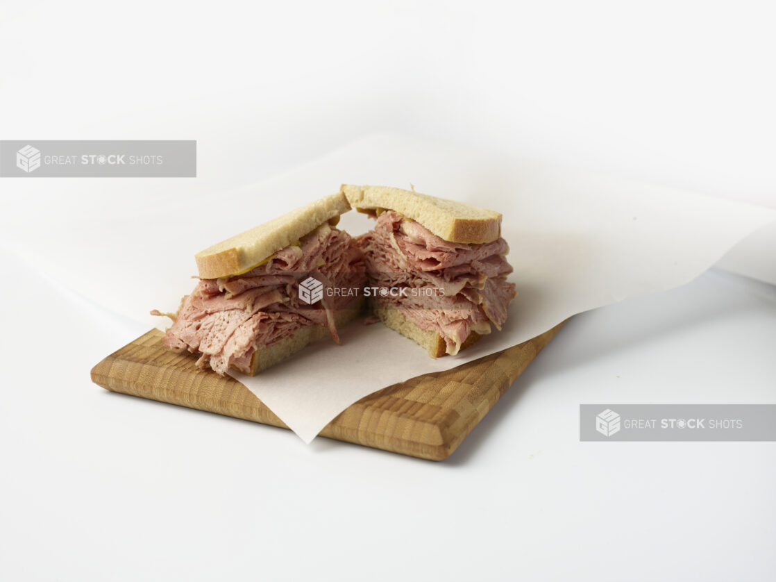 Corned beef sandwich on rye bread cut in half on a wooden board with a white background