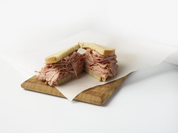 Corned beef sandwich on rye bread cut in half on a wooden board with a white background