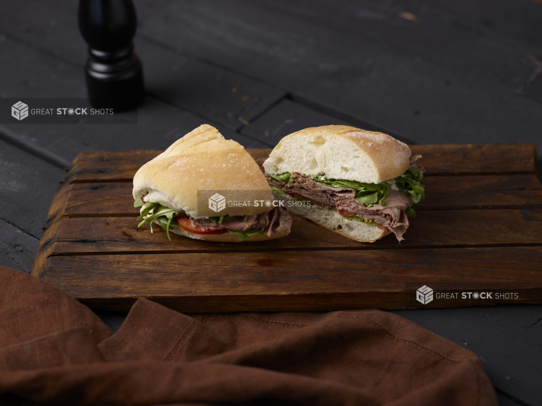 Roast beef sandwich on a white bun cut in half on a wooden board