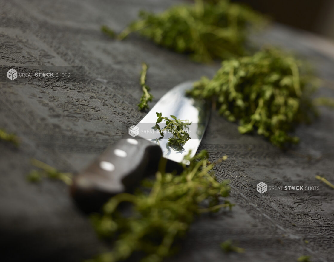 Wooden handle chefs knife with chopped fresh thyme on a black table cloth, close-up, low angle