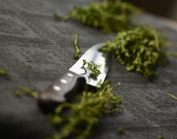 Wooden handle chefs knife with chopped fresh thyme on a black table cloth, close-up, low angle
