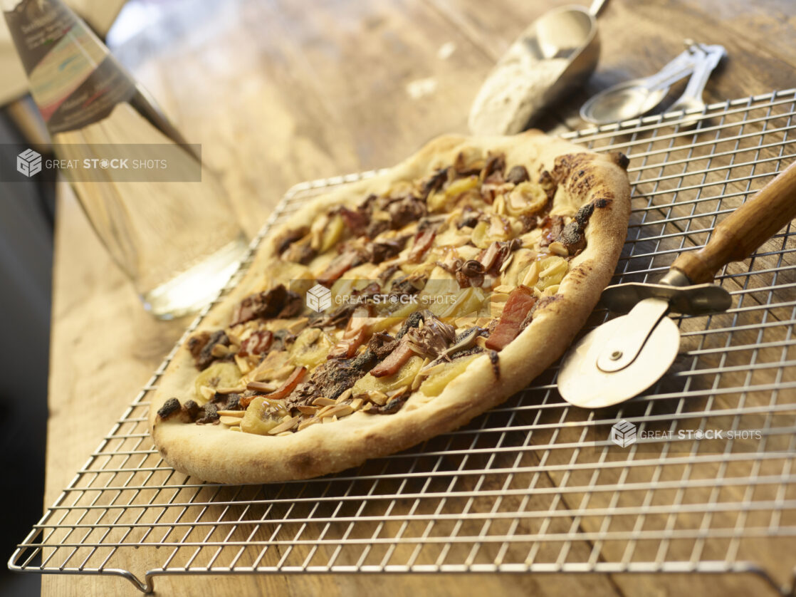 Meat bacon pizza on a cooling rack beside pizza cutting wheel