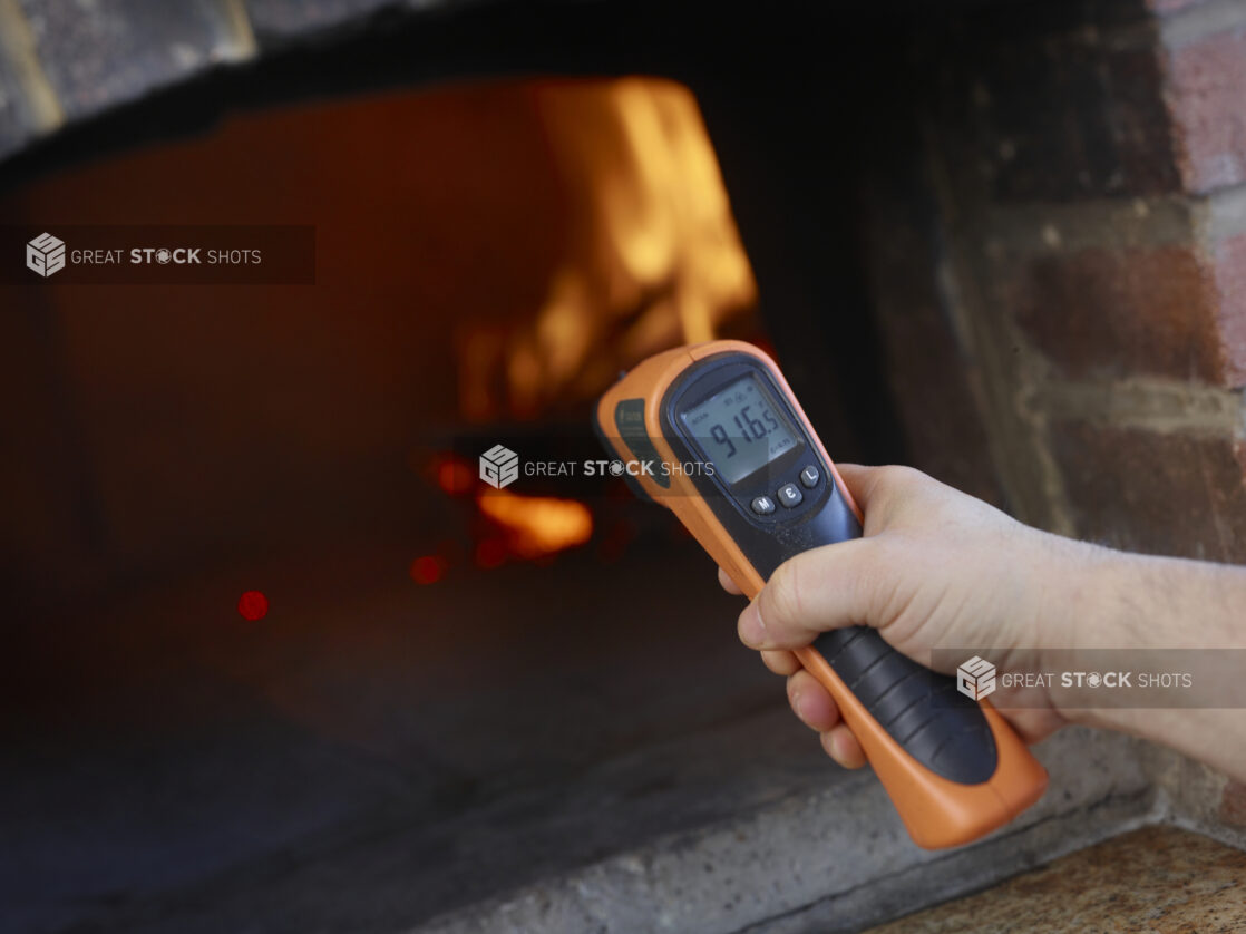 Man holding an infrared thermometer gun to measure the perfect temperature for a wood fire oven