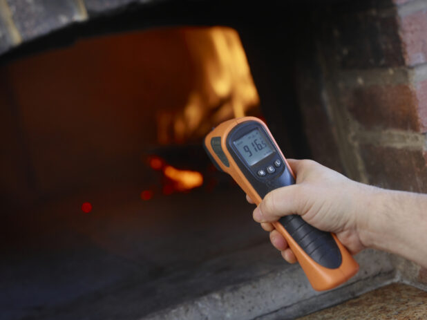 Man holding an infrared thermometer gun to measure the perfect temperature for a wood fire oven