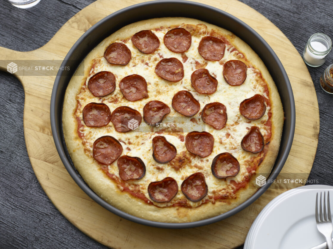 Overhead view of a full deep dish pepperoni pizza on a wooden peel on a black wooden background