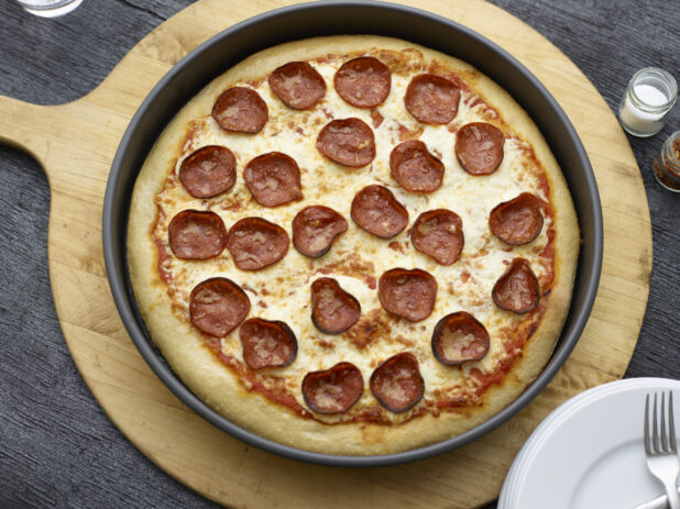Overhead view of a full deep dish pepperoni pizza on a wooden peel on a black wooden background