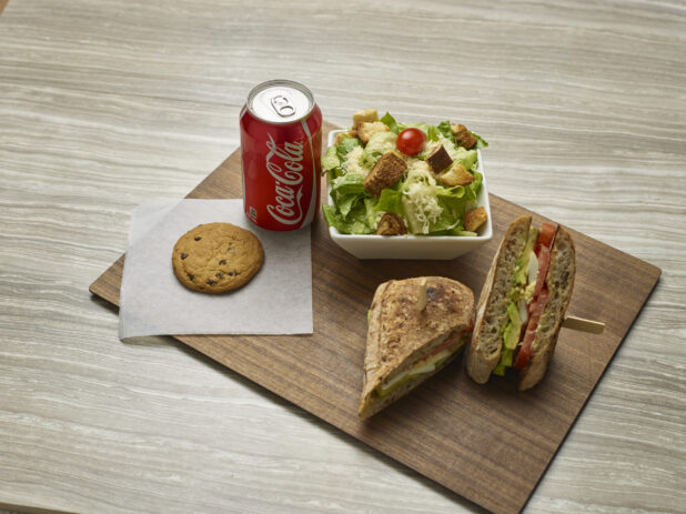 Vegetarian sandwich combo with a side caesar salad, chocolate chip cookie and can of Coke on a wooden board