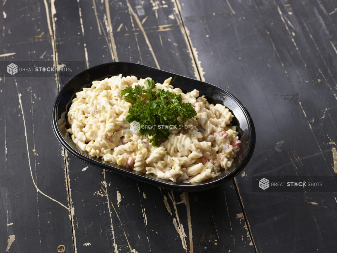 Black bowl of pasta salad garnished with parsley on a distressed black wooden background