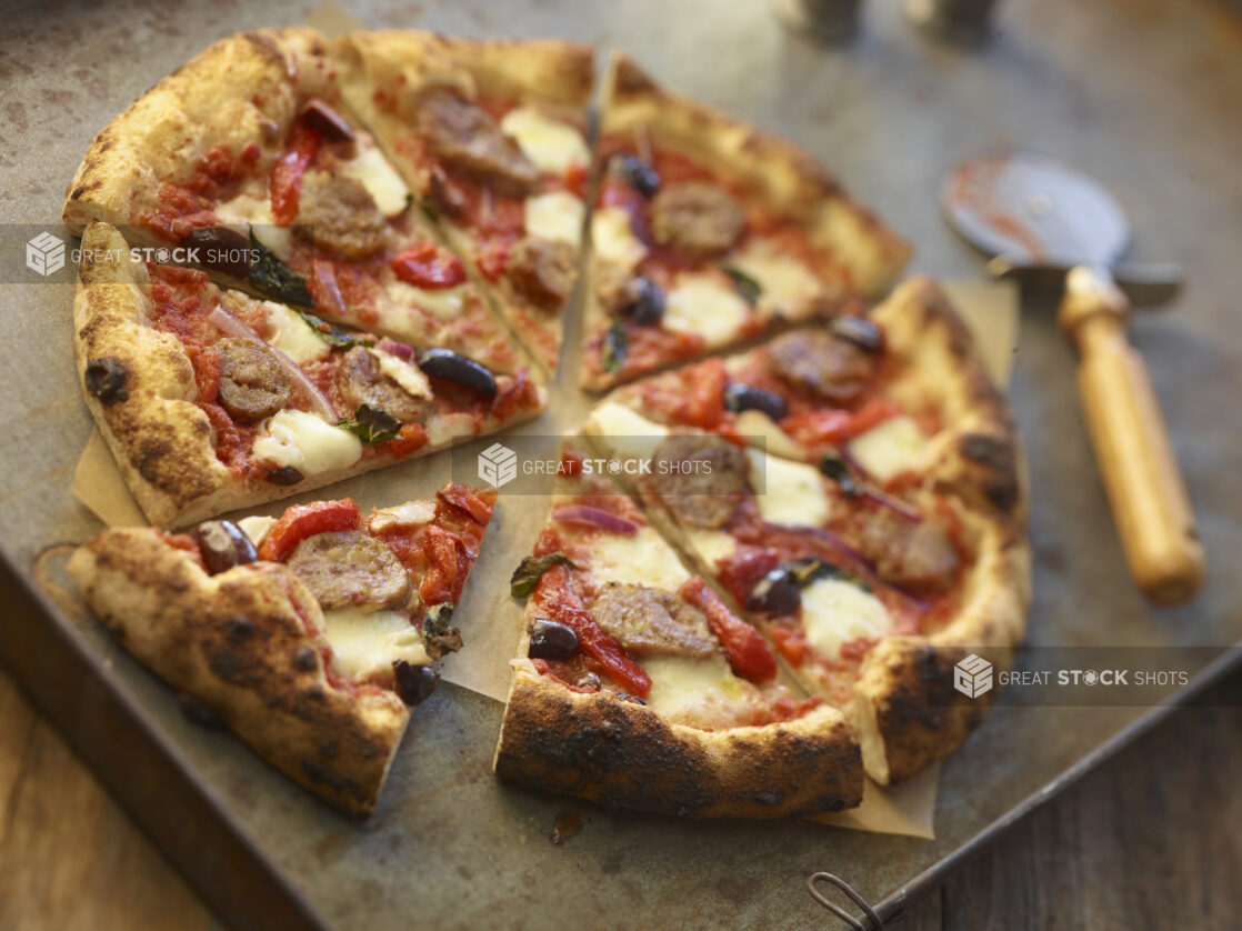 Sliced four-topping pizza on a metal board with a pizza cutter