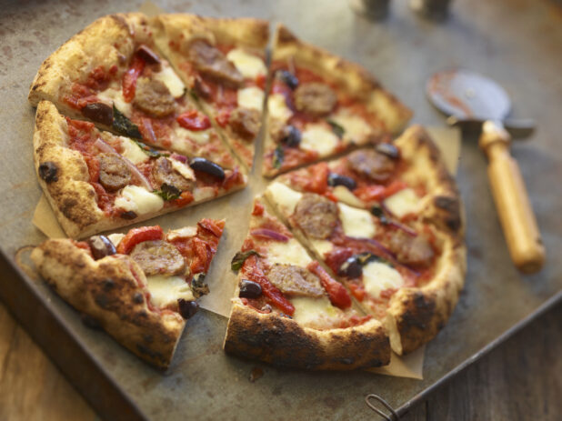 Sliced four-topping pizza on a metal board with a pizza cutter