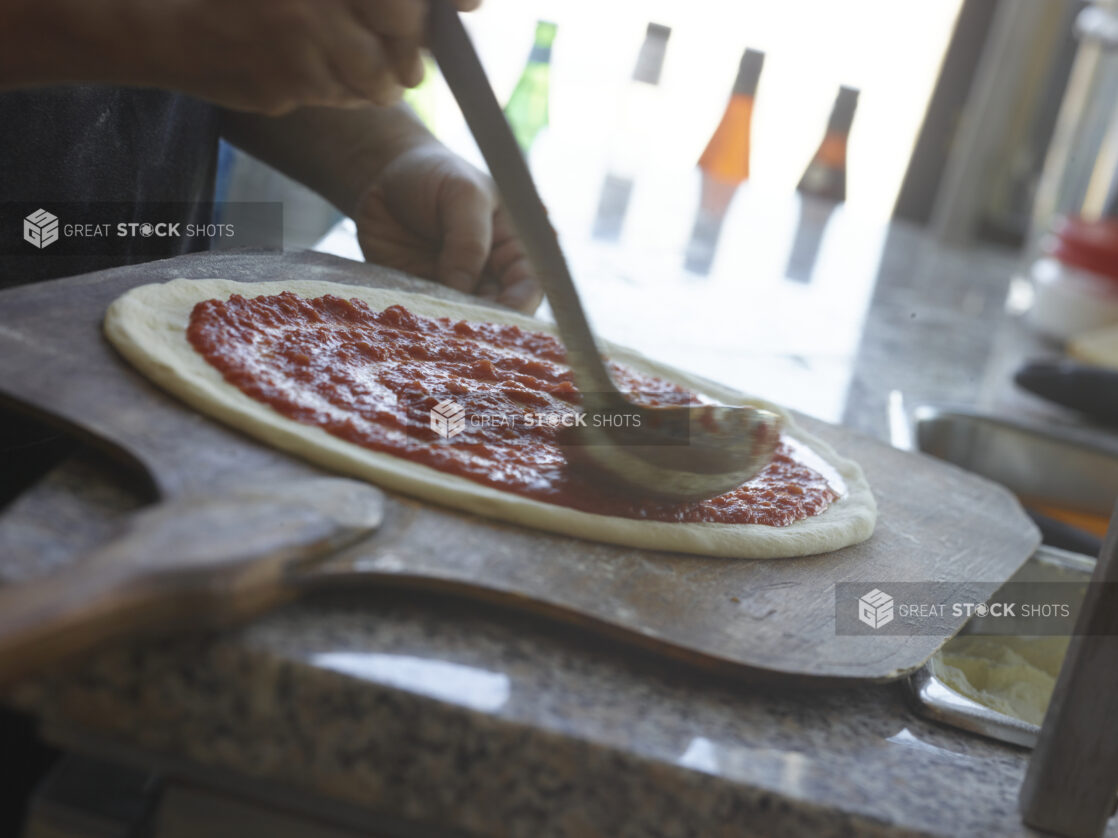 Pizza chef spreading tomato sauce around pizza dough on a peel in a restaurant