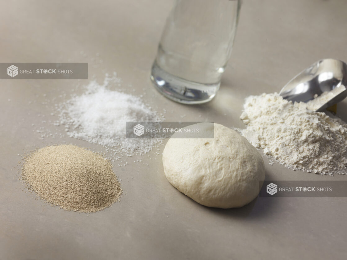 White dough ball surrounded by dough ingredients on a beige background