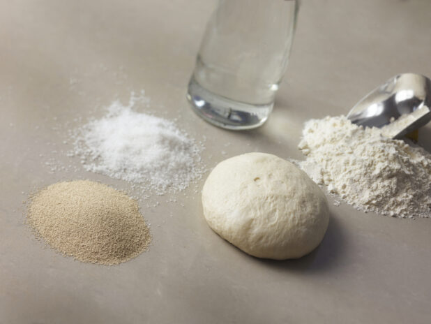 White dough ball surrounded by dough ingredients on a beige background