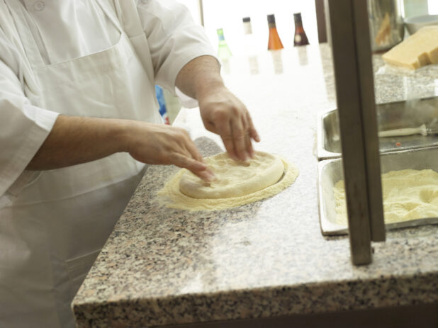 Pizza chef forming a pizza crust on a cornmeal-coated marble work surface