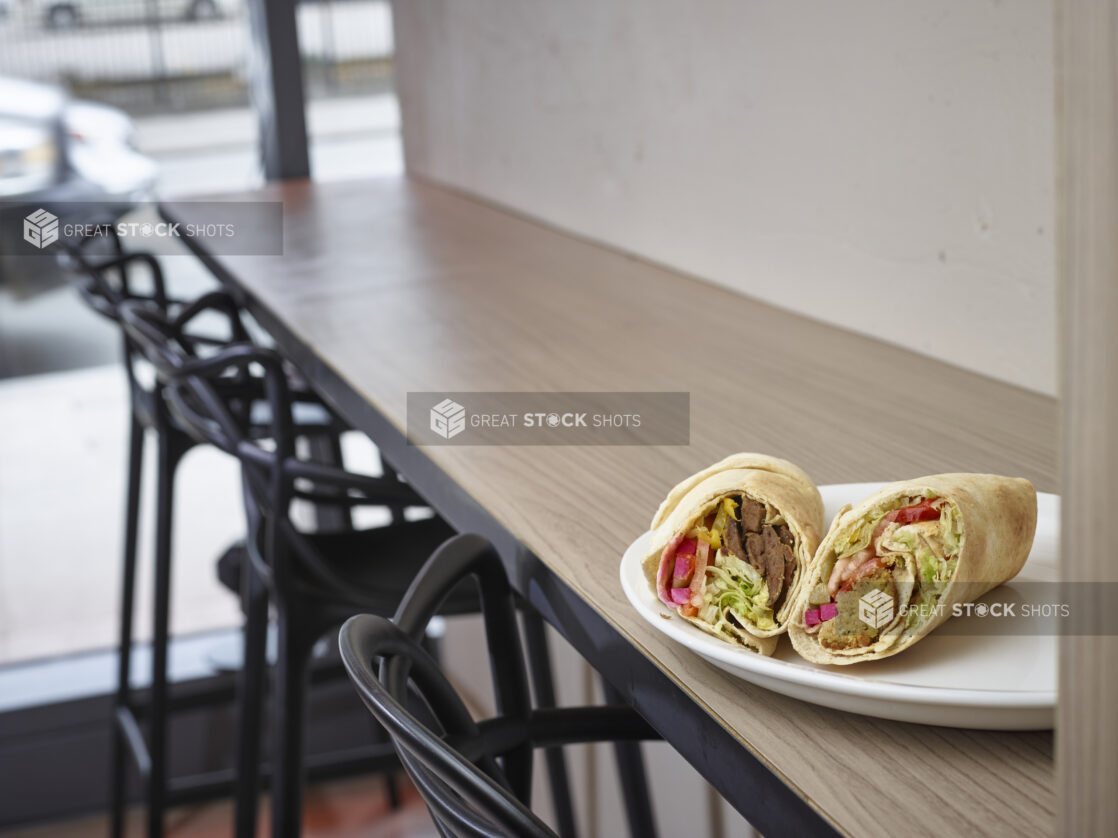 Middle eastern gyro and falafel pita on a plate sitting on top of a wooden table in a restaurant