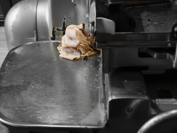 Commercial meat slicer shaving turkey breast in a restaurant