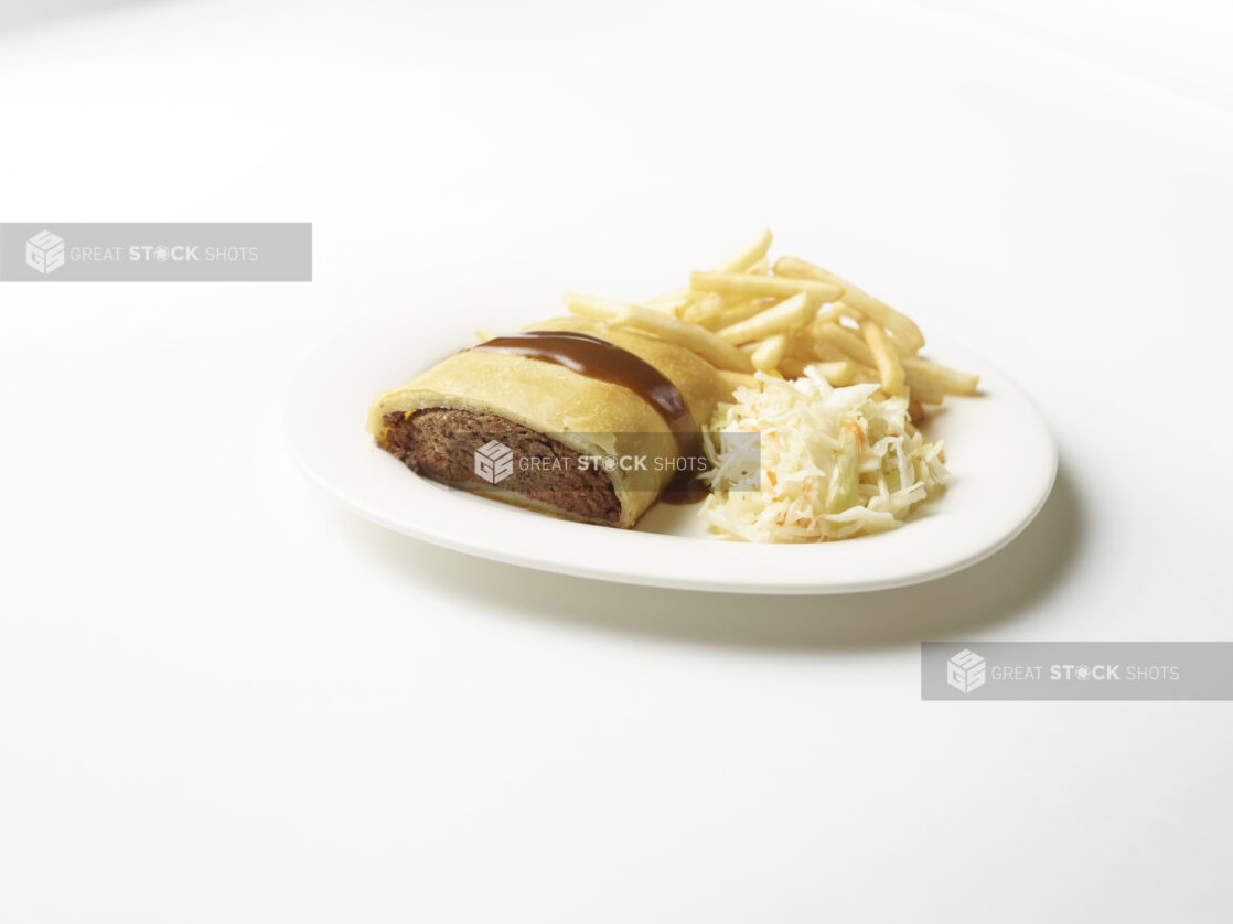 White plate of knish with a side of french fries and coleslaw on a white background